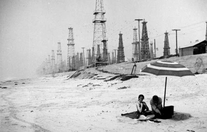 A couple spread out a picnic in the shadows of Huntington Beach oil derricks, circa 1937