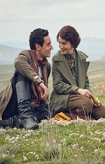 A young man and a young woman sit on a hillside, talking. 