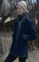 A warmly dressed woman stands alone next to a large tree. 
