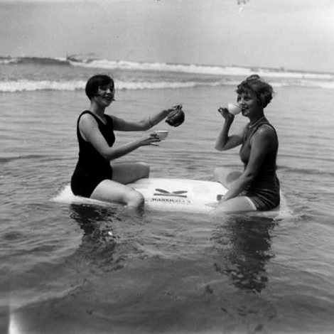 Two young women are sitting on a raft as they drink tea in the ocean at Venice beach.