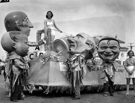 Mardi Gras parade of 1936 at Venice Beach showing one float with giant characters in masks standing beside the float while one young lady in a swim suit stands atop it.