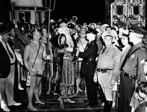 Mardi Gras parade of 1936 at Venice Beach showing a crowd gathered around Neptune and his assistants as he receives the key to the city from the Venice Chamber of Commerce representative.