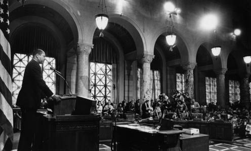 Mayor Bradley stands at the podium addressing the press, officials and a room full of people.