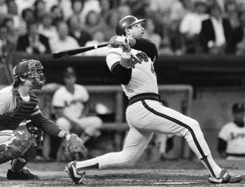 Baseball player Reggie Jackson at bat, hitting the ball to centerfield.