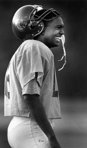 Black and white sideview photo of quarterback Rodney Peete smiling on the field.