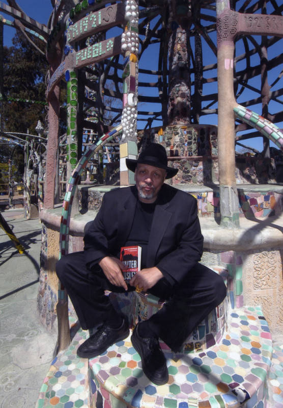 Author Walter Mosley holding a paperback copy of his book "Little Scarlet" at the Watts Towers..