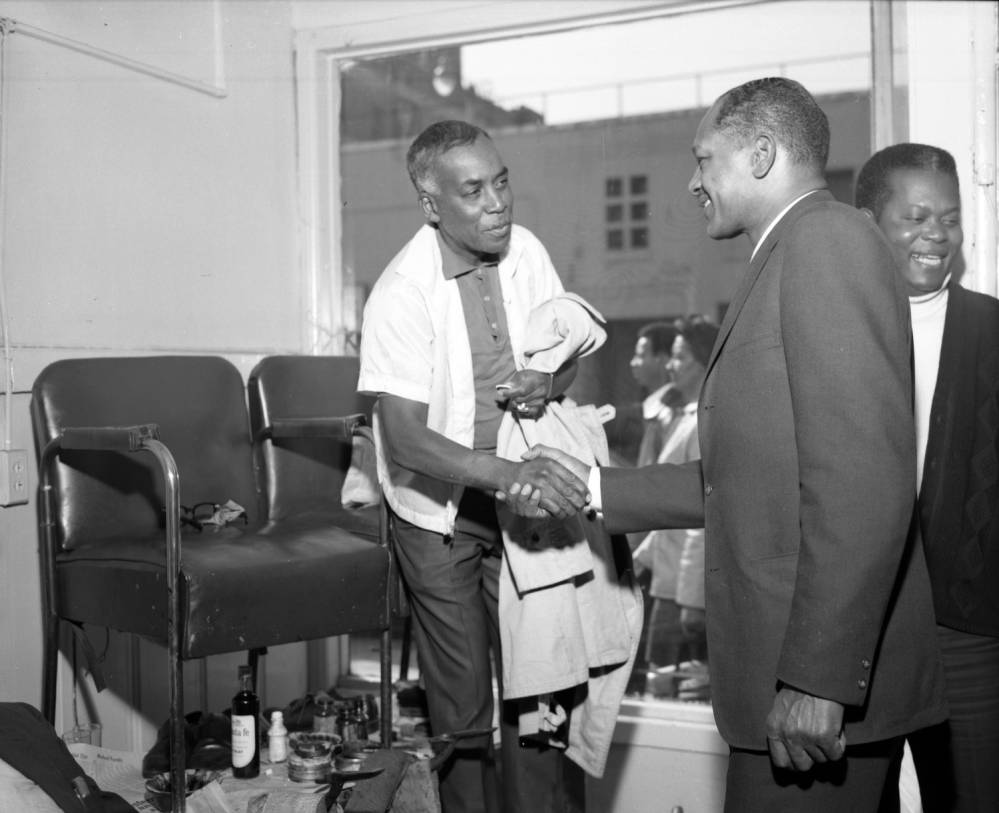 	 Councilmember Tom Bradley (in suit) is shown shaking hands with an unidentified man at a shoe shine station