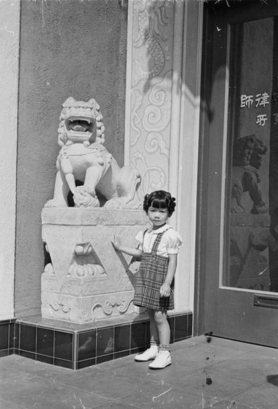A little girl poses next to the lion statue in front of the Y. C. Hong Building in New Chinatown