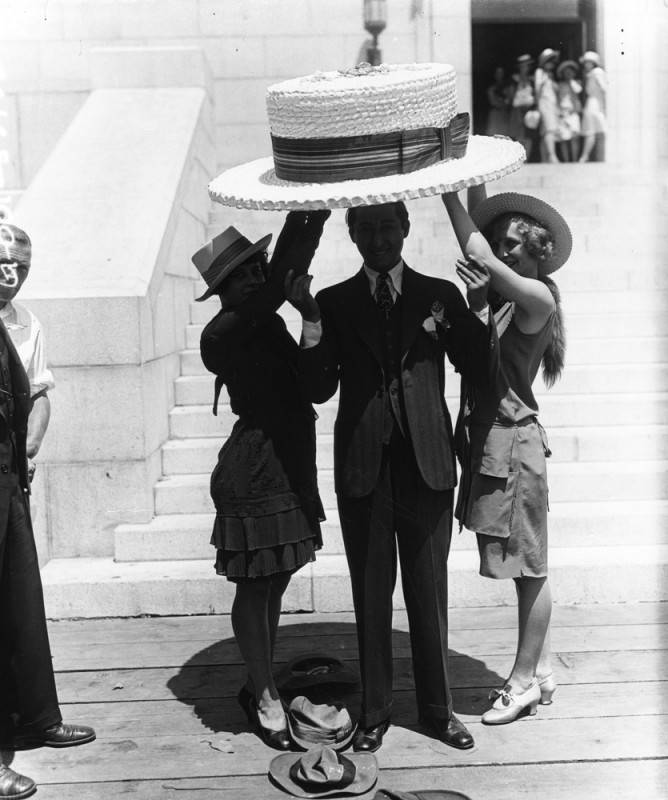 2 ladies holding up a giant straw hat over the Mayor