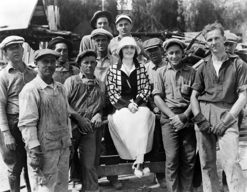 Poli Negri sitting in the middle of a group of construction workers