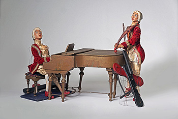 color photo of puppets of two musicians in red robes with white wigs on a piano