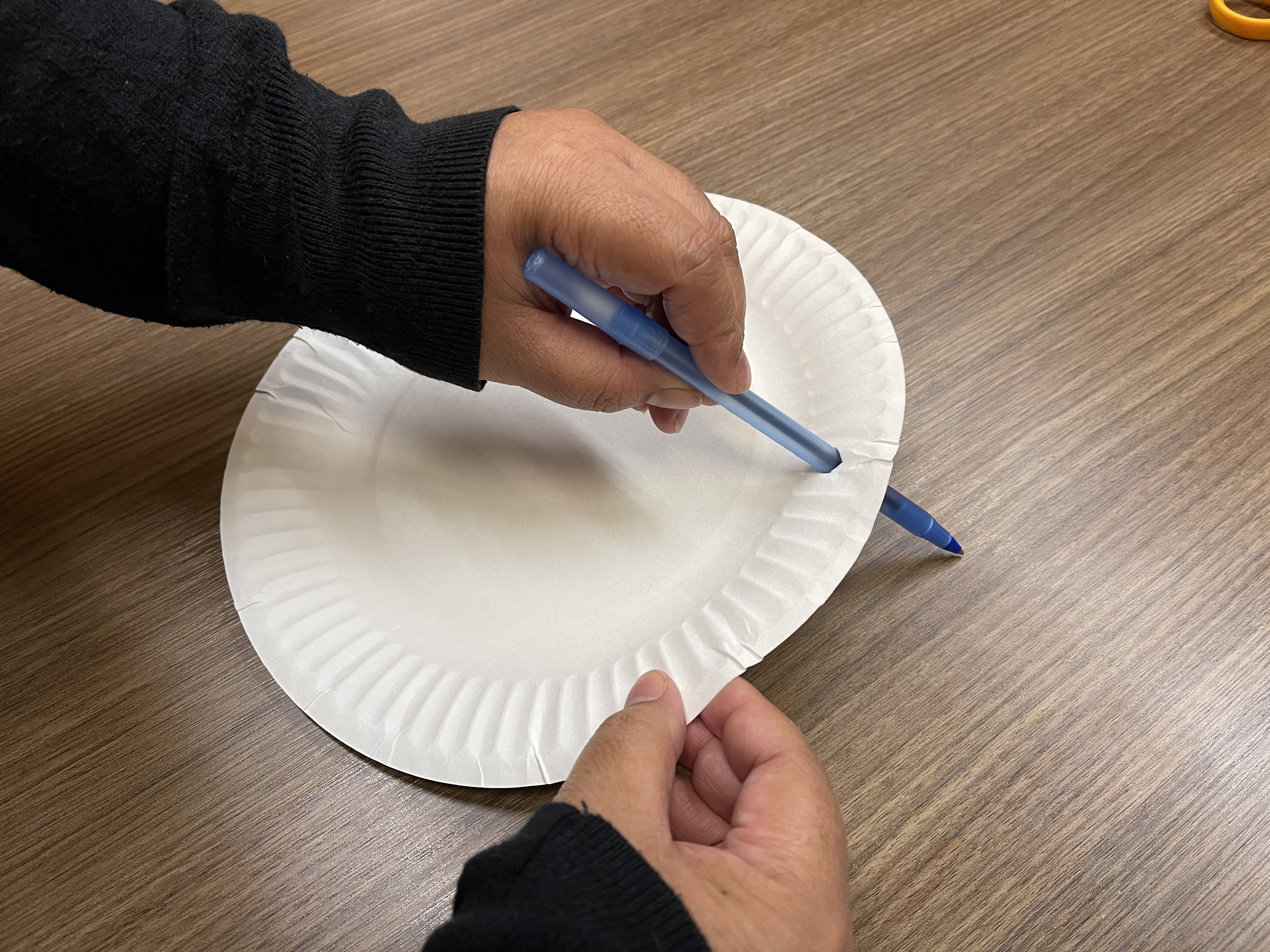 a pen punching a hole through a paper plate