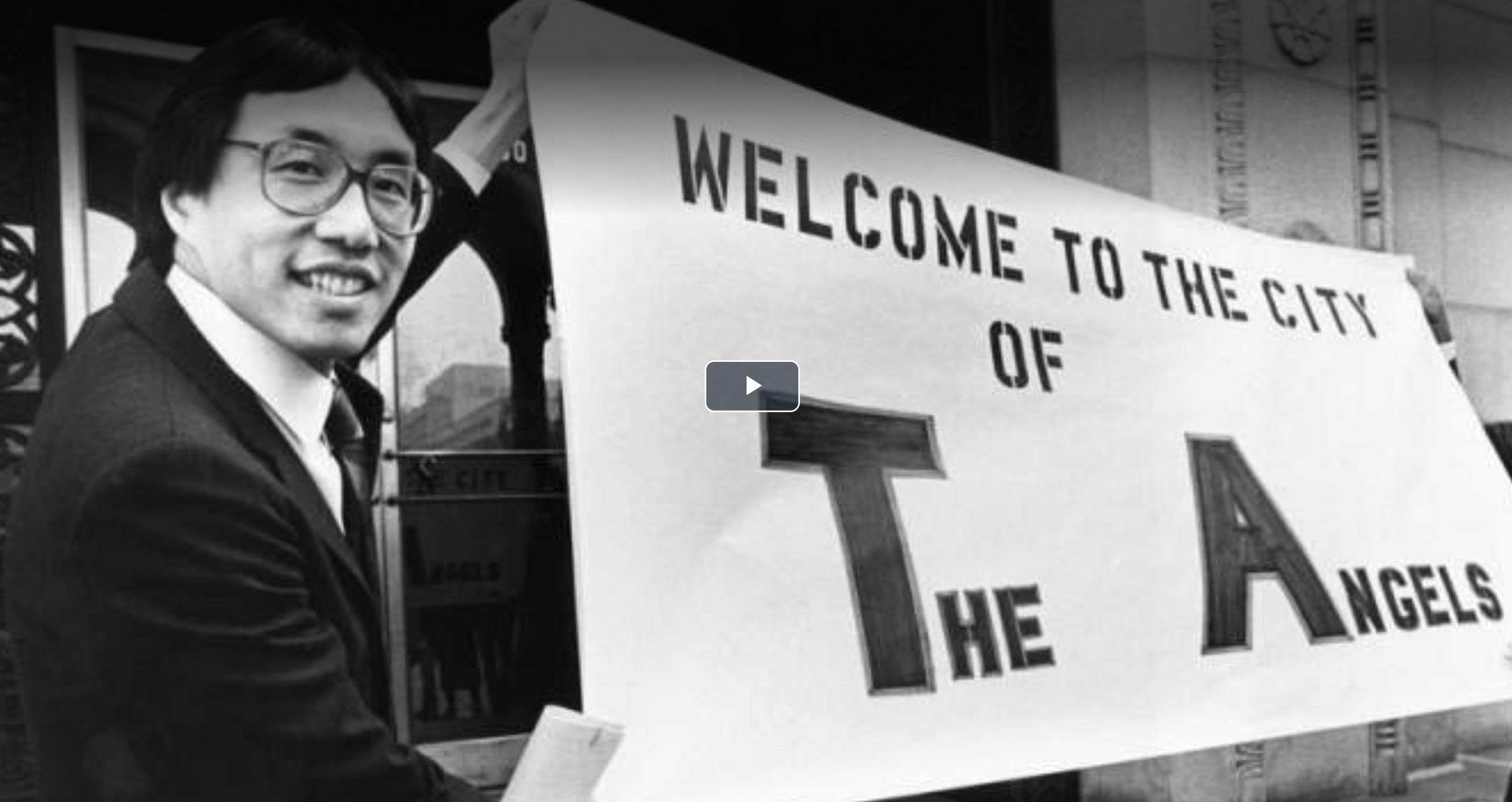 black and white photo of Michael Woo with sign 'welcome to the city of angels'