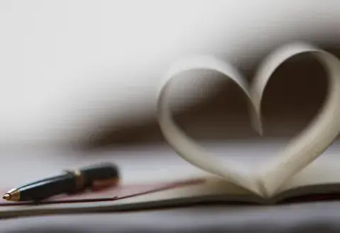 A black pen rests on an open book with pages folded to resemble a heart shape.