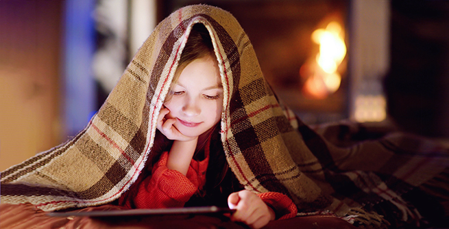 Young girl reading under a warm blanket