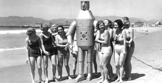 Robot on the beach surrounded by ladies in bathing suits