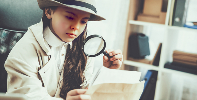 Young girl investigating photos with magnifying glass.