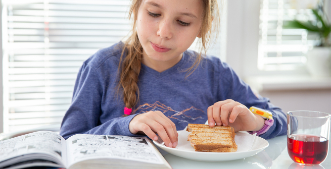 Girl reads a graphic novel while having a grilled ham and cheese sandwich