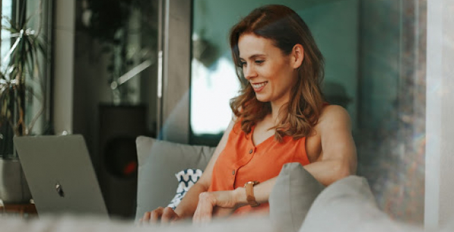 woman in an orange tank top looking at her laptop on the couch