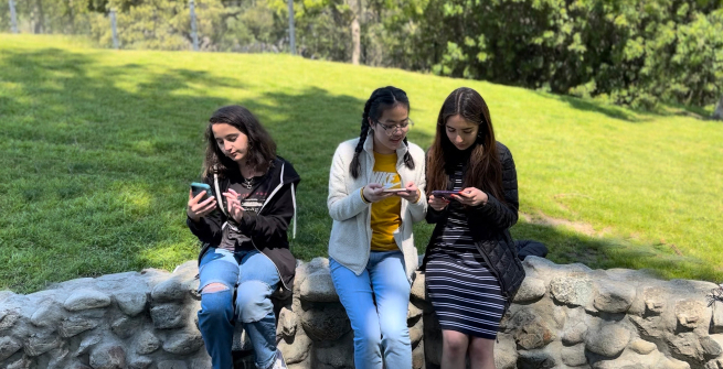 3 teens looking at their phones in a park