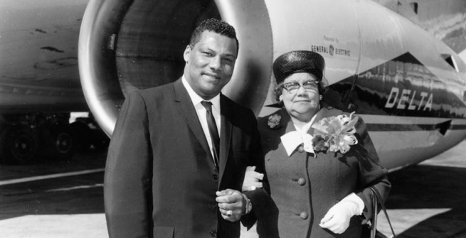 Photographer Rolland J. Curtis and his mother, Mathilda Curtis. They are standing near a Delta Airlines plane, and she is wearing a corsage.