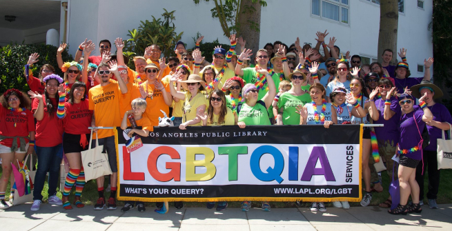 Librarians wearing rainbow colored tshirts in front of a LGBTQIA banner
