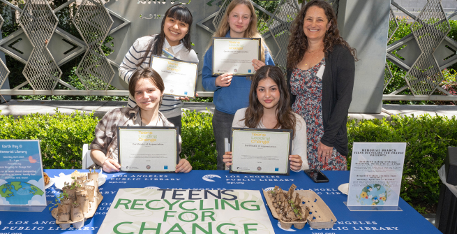 Four teen volunteers hold up their certificates next to librarian