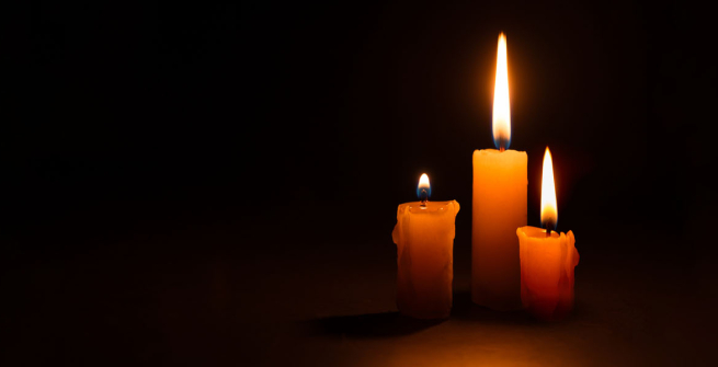Three burning taper candles against a black background.