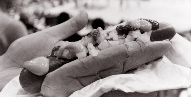 An oversized hot dog fills the bun which is topped with mustard, ketchup and onions.