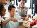 Young boy cutting vegetables with the family watching
