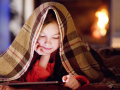 Young girl reading under a warm blanket