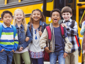 Happy, laughing diverse tweens standing near a school bus