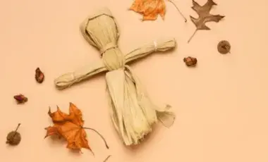 A corn husk doll surrounded by dried leaves