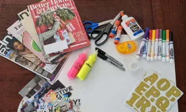 White poster board surrounded by colored pens, glue, a pile of magazines and words cut out of magazines