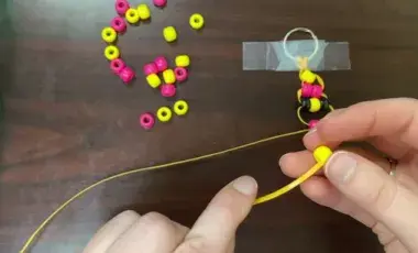 hands putting beads onto a plastic string
