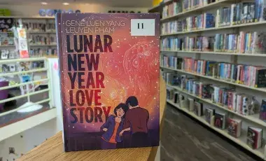Image of library stacks and close up of book with two people and red and orange colors on the cover. 