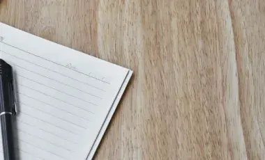 a blank notepad is open with a black pen resting on it and a pair of glasses above the notepad