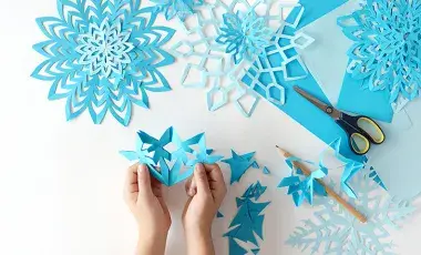 small hands holding a paper cut out of a snowflake 
