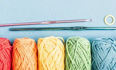 Six balls of yarn of various colors with two crochet needles on a blue background