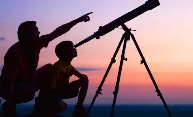 Man with child and telescope looking at the night sky