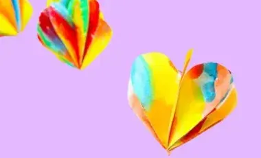 Multicolored 3D paper hearts on a pink background. 