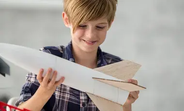 A smiling girl holds a spaceship made of paper in her hands.