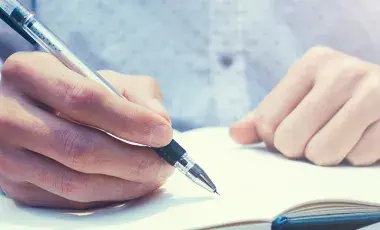 Open blank book with two hands, one holding pen.