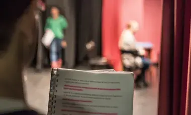 person reads a script while standing backstage in a theater