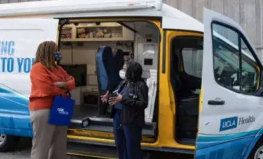 Two people talking outside of a branded UCLA Health van