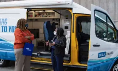 two people standing in front of the UCLA mobile health van