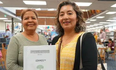 Two smiling women holding reading workbook.