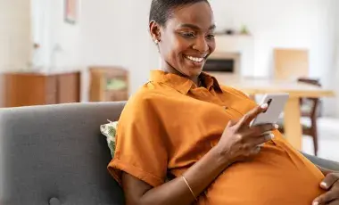 pregnant woman in orange shirt smiling and looking at phone