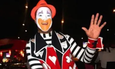 An adult clown waving his left hand.