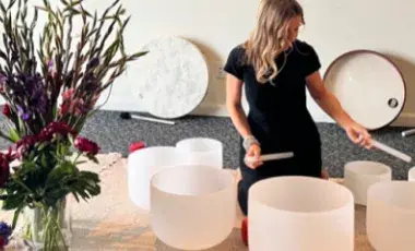 Healing practitioner making sounds with crystal bowls next to a large bouquet